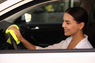 Photo of Young woman cleaning steering wheel with rag in car, view from outside