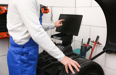 Mechanic working with wheel balancing machine at tire service, closeup