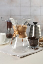 Photo of Empty glass chemex coffeemaker with and beans on white table