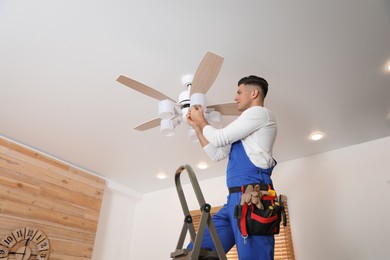 Photo of Electrician changing light bulb in ceiling fan indoors