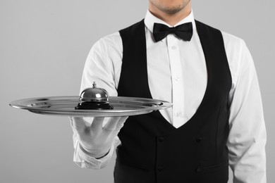 Butler holding metal tray with service bell on grey background, closeup