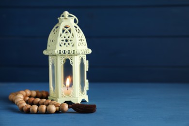 Decorative Arabic lantern and prayer beads on blue wooden table. Space for text