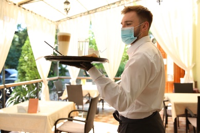 Photo of Waiter serving beverages in restaurant. Catering during coronavirus quarantine