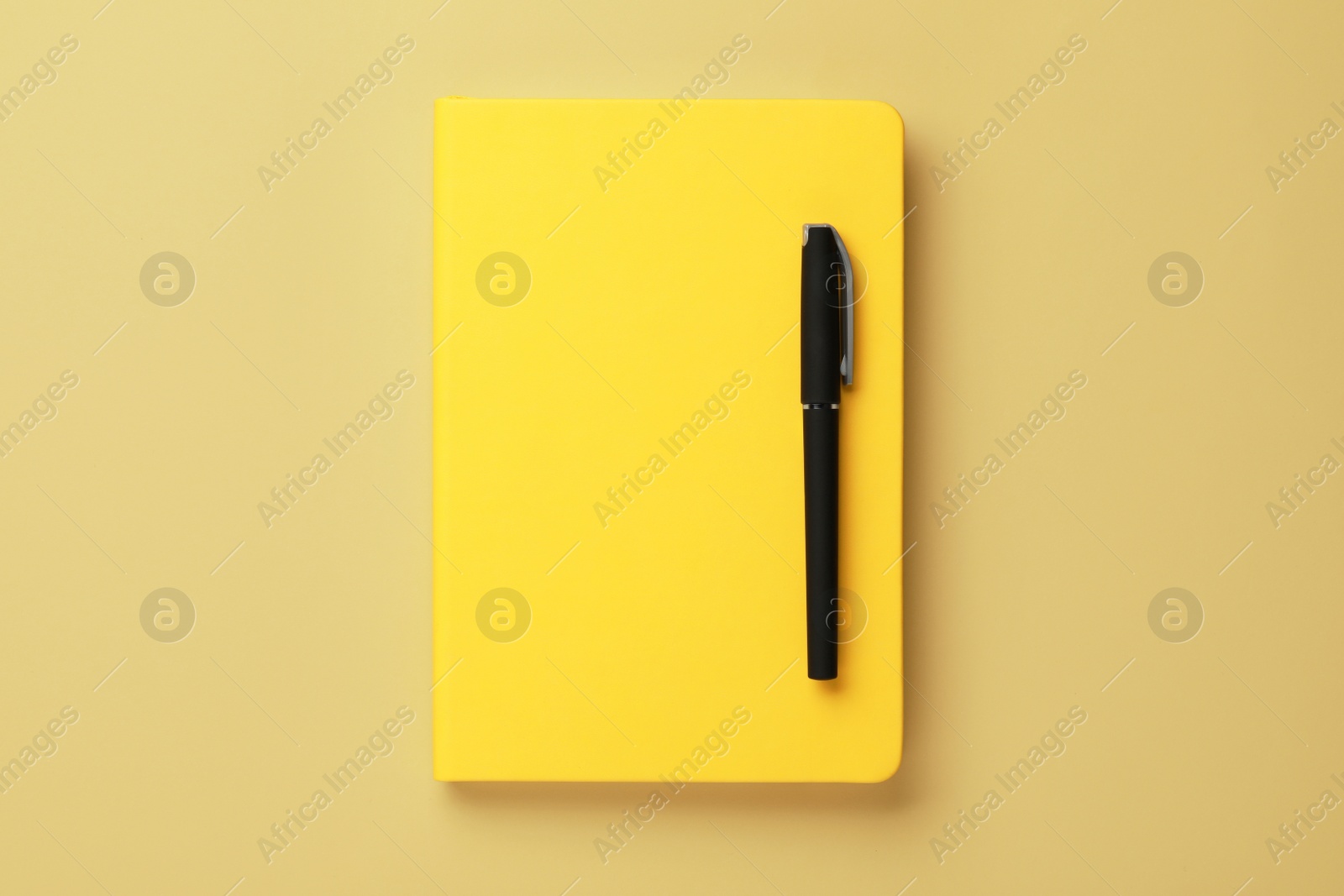 Photo of Notebook and pen on pale yellow background, top view