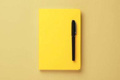 Notebook and pen on pale yellow background, top view