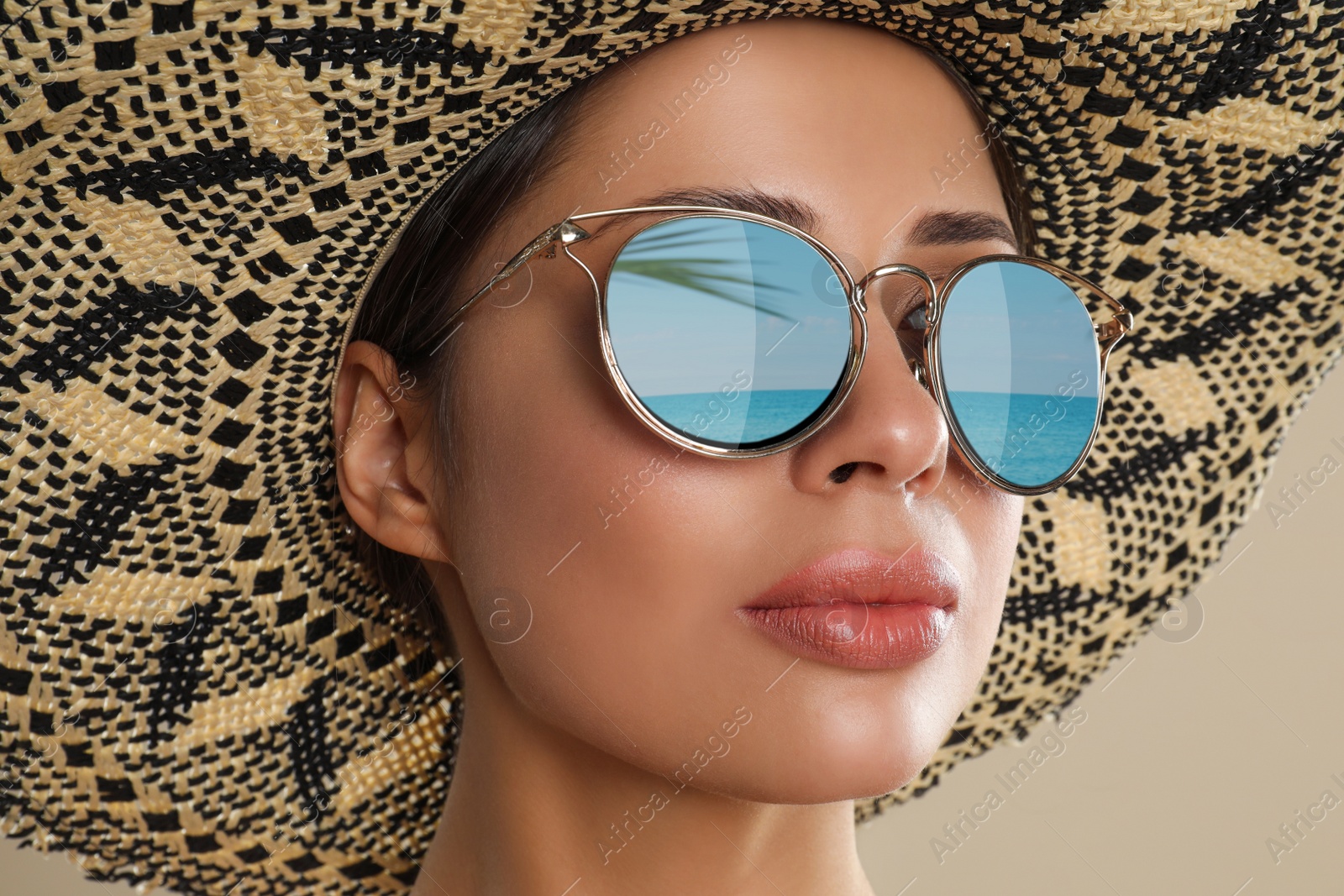 Image of Beautiful young woman wearing sunglasses with reflection of sea and hat on beige background 