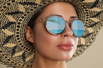 Image of Beautiful young woman wearing sunglasses with reflection of sea and hat on beige background 