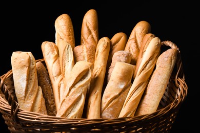 Photo of Fresh tasty baguettes in basket against black background, closeup