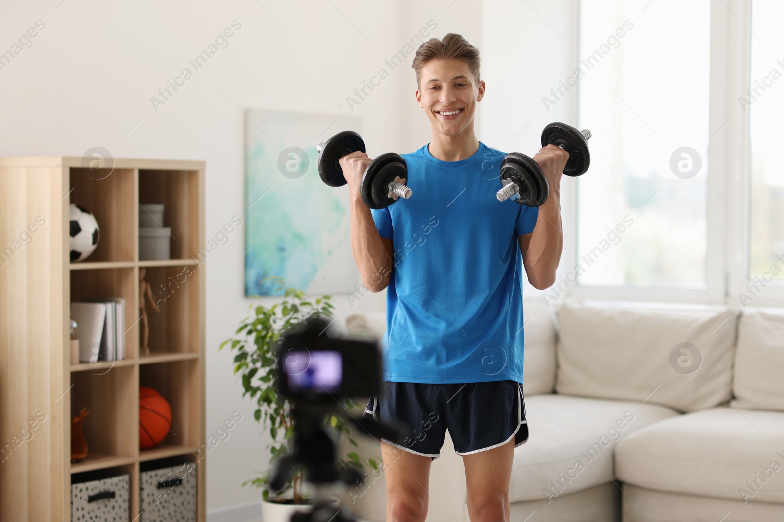 Photo of Smiling sports blogger working out with dumbbells while recording fitness lesson at home