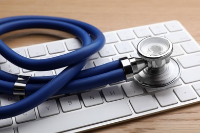 Photo of Computer keyboard with stethoscope on wooden table, closeup