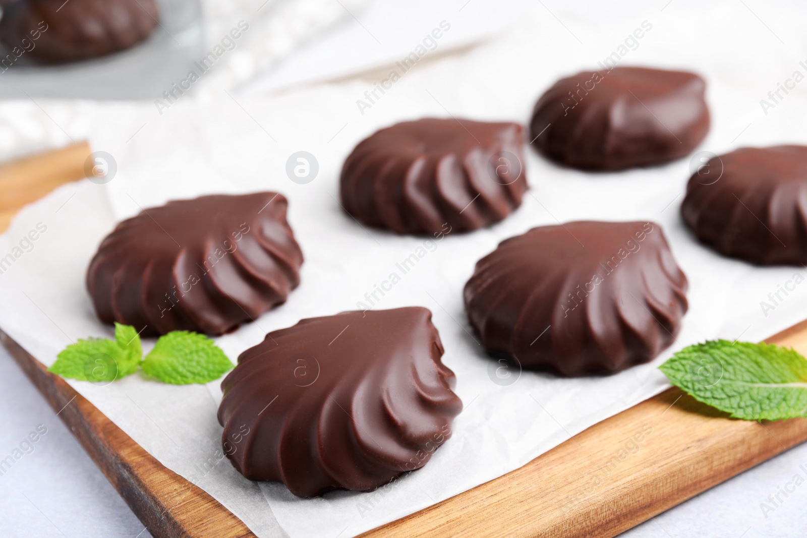 Photo of Delicious chocolate covered zephyrs and mint on wooden board, closeup