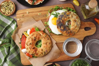 Tasty bagel sandwiches on brown table, flat lay