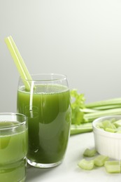 Glass of delicious celery juice and vegetables on white table