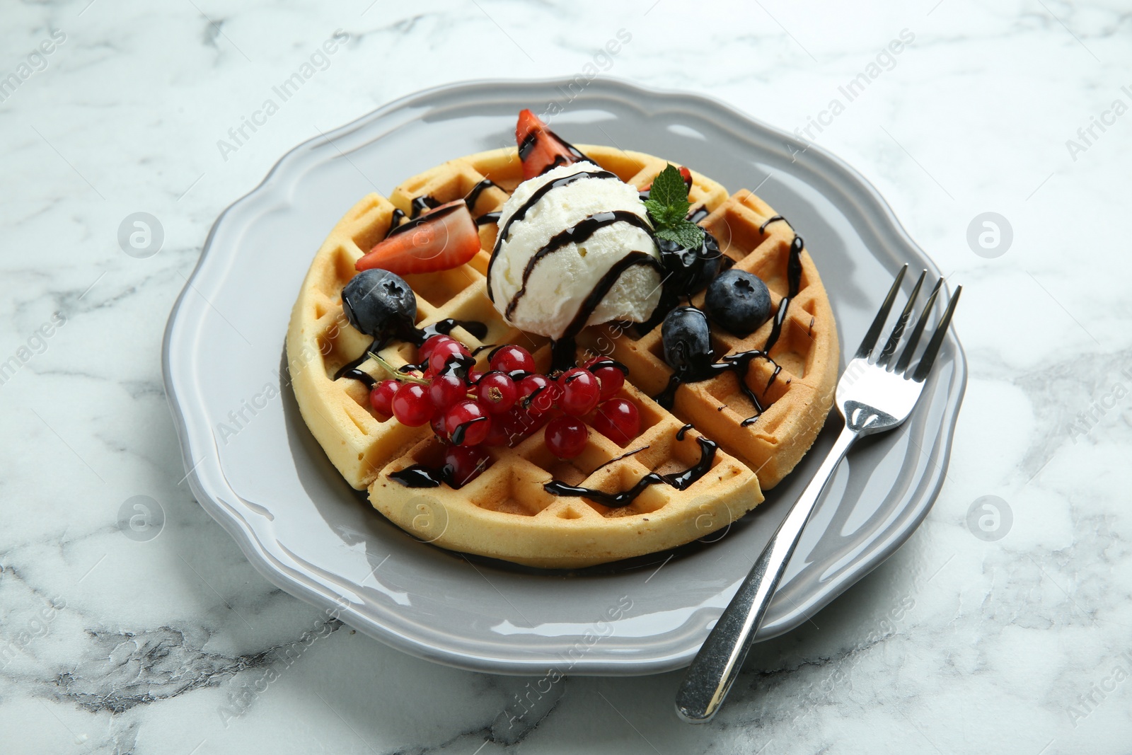 Photo of Delicious Belgian waffles with ice cream, berries and chocolate sauce on light marble table, closeup