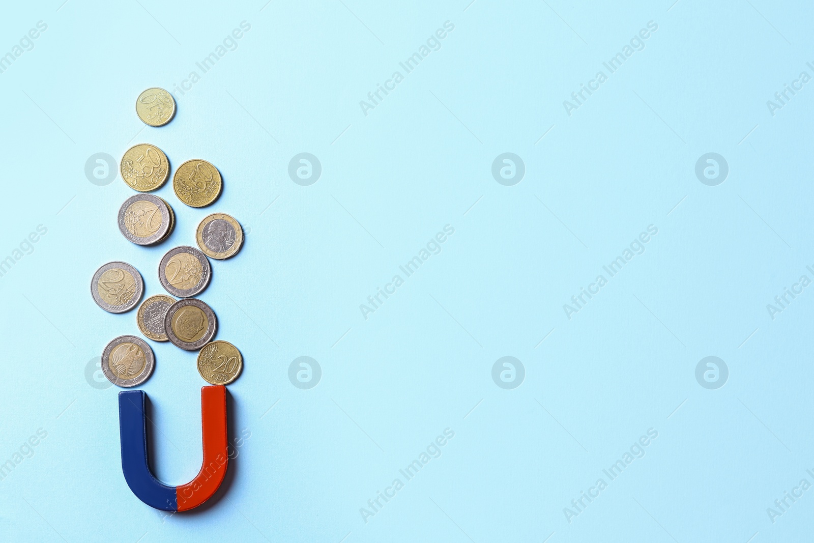 Photo of Red and blue horseshoe magnet attracting coins on light blue background, flat lay. Space for text