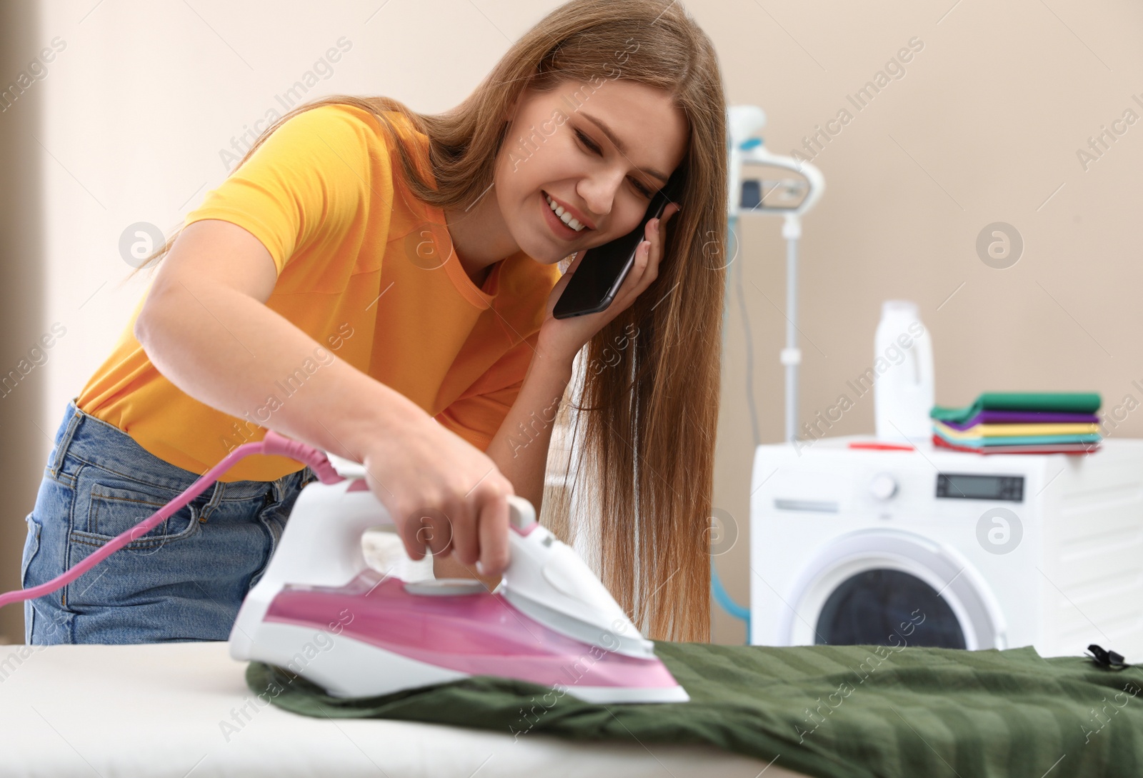 Photo of Happy woman talking on phone while ironing clothes in bathroom. Space for text