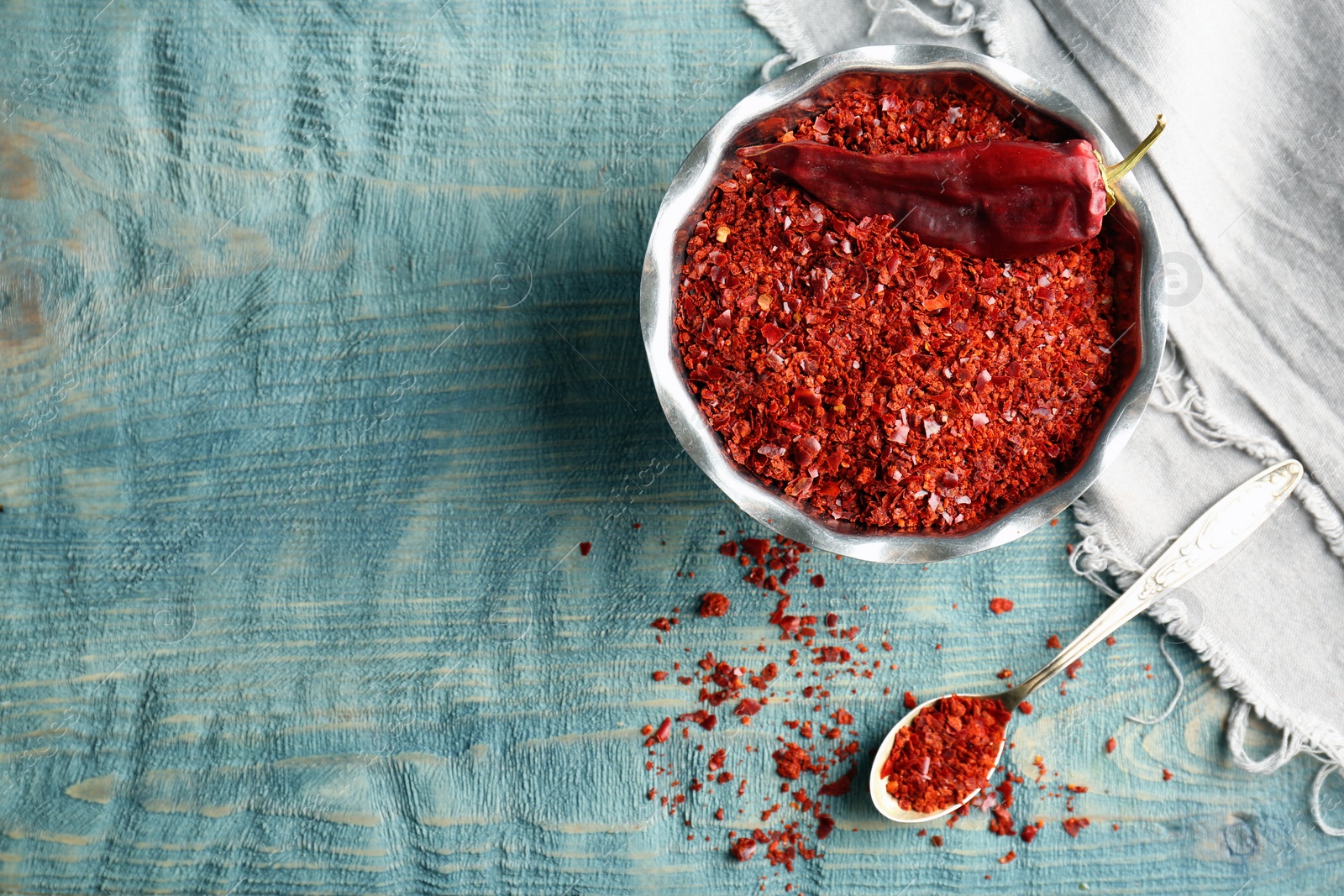 Photo of Bowl with crushed chili pepper and pod on wooden background