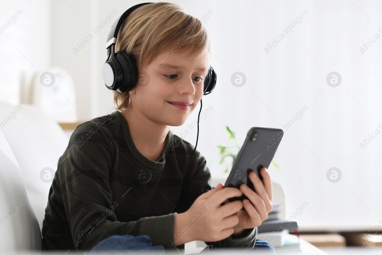 Photo of Cute little boy with headphones and smartphone listening to audiobook at home