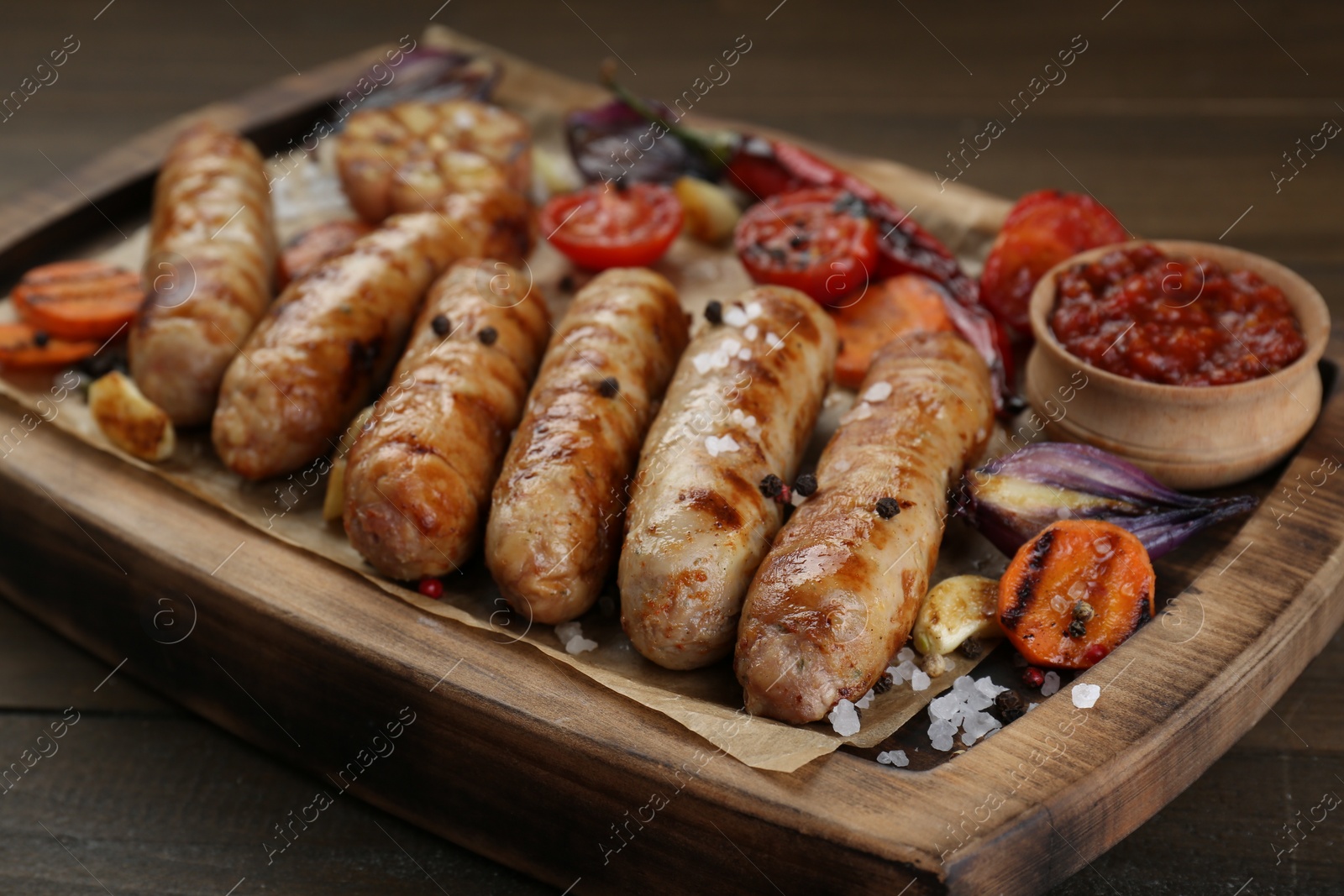 Photo of Tasty grilled sausages with vegetables on wooden table, closeup