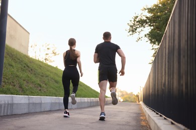 Photo of Attractive sporty couple in fitness clothes jogging outdoors, back view