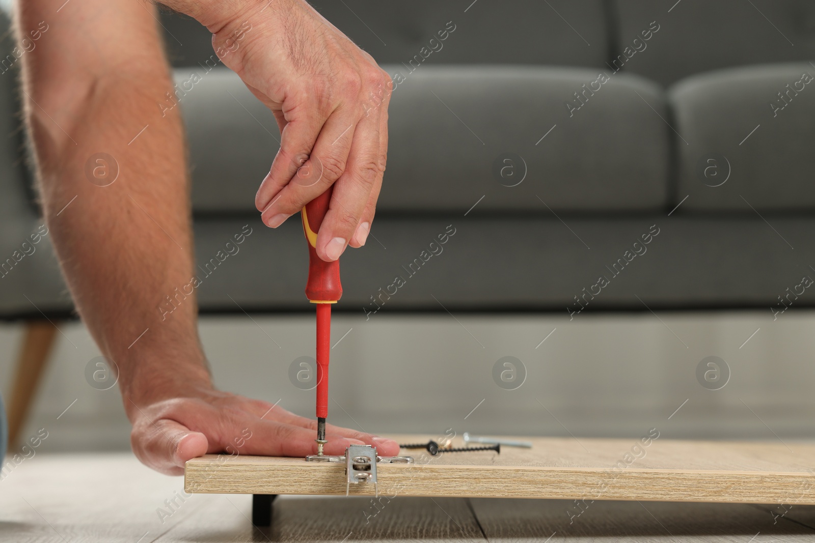 Photo of Man with screwdriver assembling furniture on floor indoors, closeup. Space for text