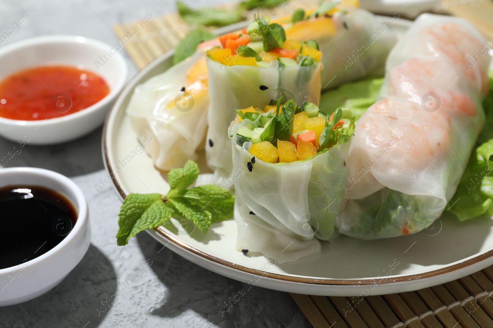 Photo of Tasty spring rolls and sauces on grey textured table, closeup