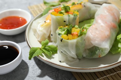 Tasty spring rolls and sauces on grey textured table, closeup