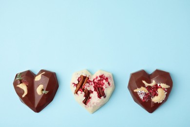 Photo of Tasty chocolate heart shaped candies with nuts on light blue background, flat lay. Space for text