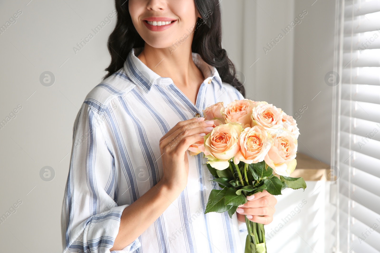 Photo of Young woman with beautiful bouquet near window at home, closeup