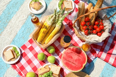 Different products for summer picnic served on checkered blanket, flat lay