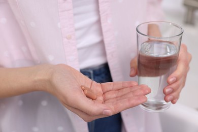 Photo of Woman with vitamin pills and glass of water indoors, closeup