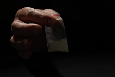 Photo of Addicted man with plastic bag of drug on dark background, closeup. Space for text