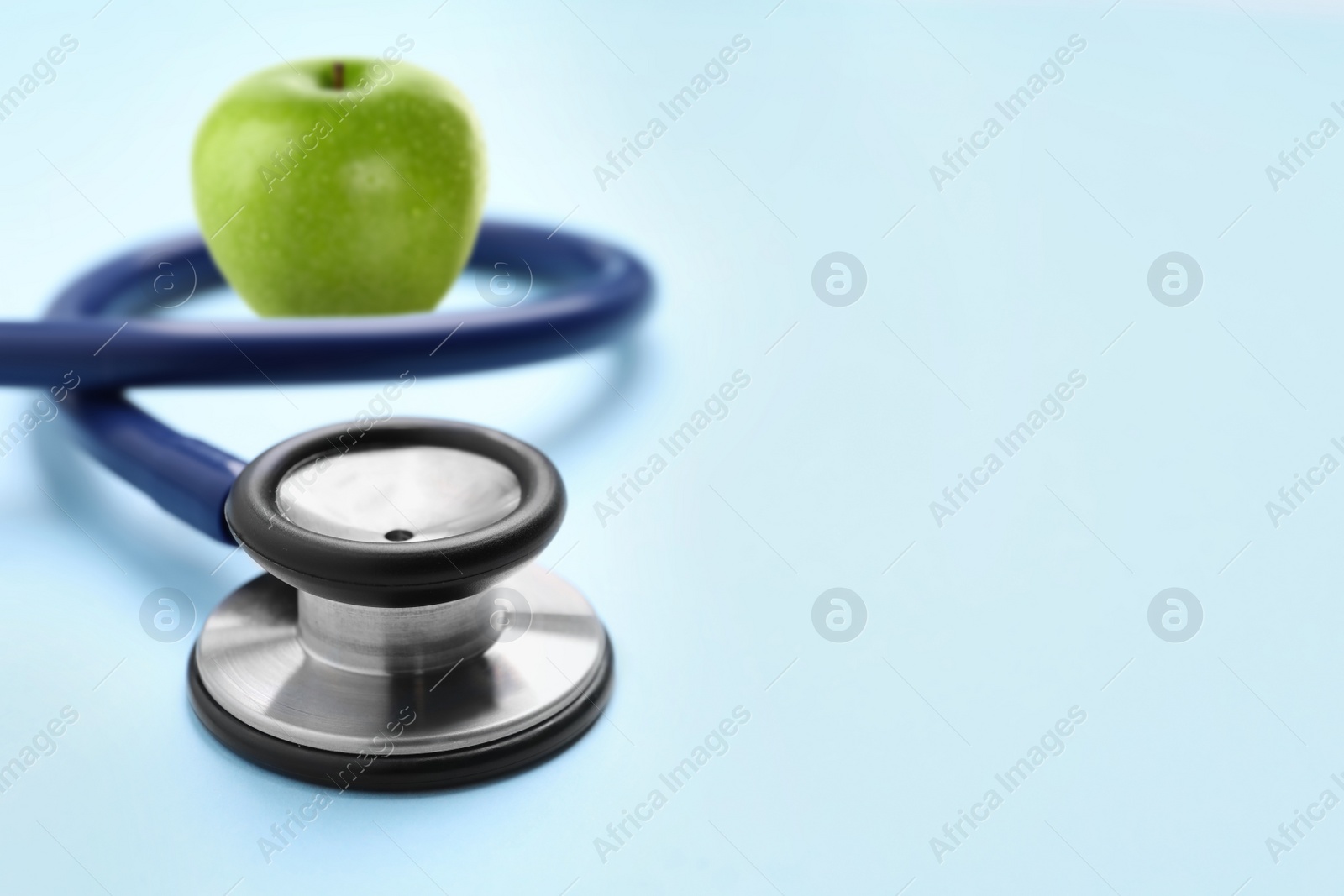 Image of Stethoscope and green apple on light blue background, space for text 