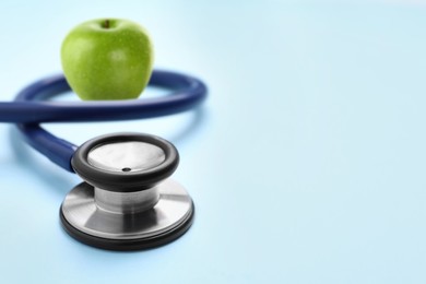 Image of Stethoscope and green apple on light blue background, space for text 