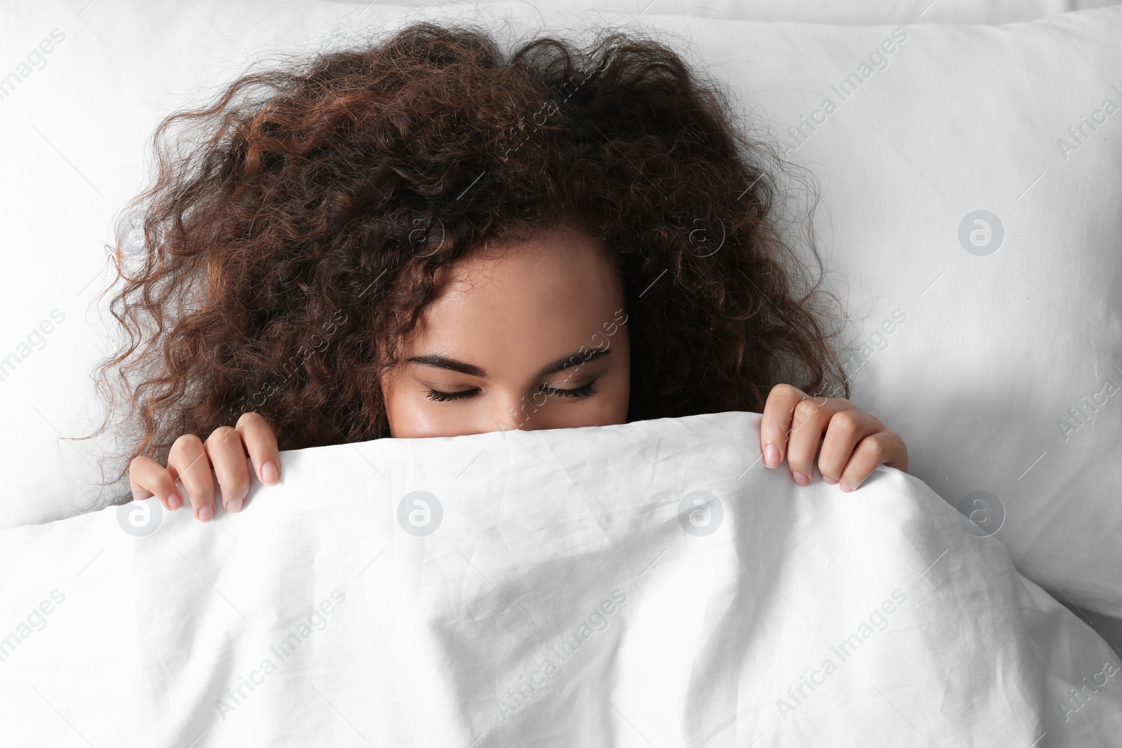 Photo of Young African-American woman sleeping on soft pillow, top view. Bedtime