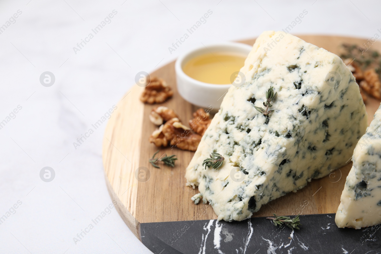 Photo of Tasty blue cheese with thyme, honey and walnuts on white marble table, closeup. Space for text