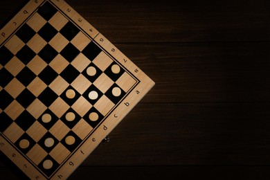 Photo of Checkerboard with game pieces on wooden table, top view. Space for text