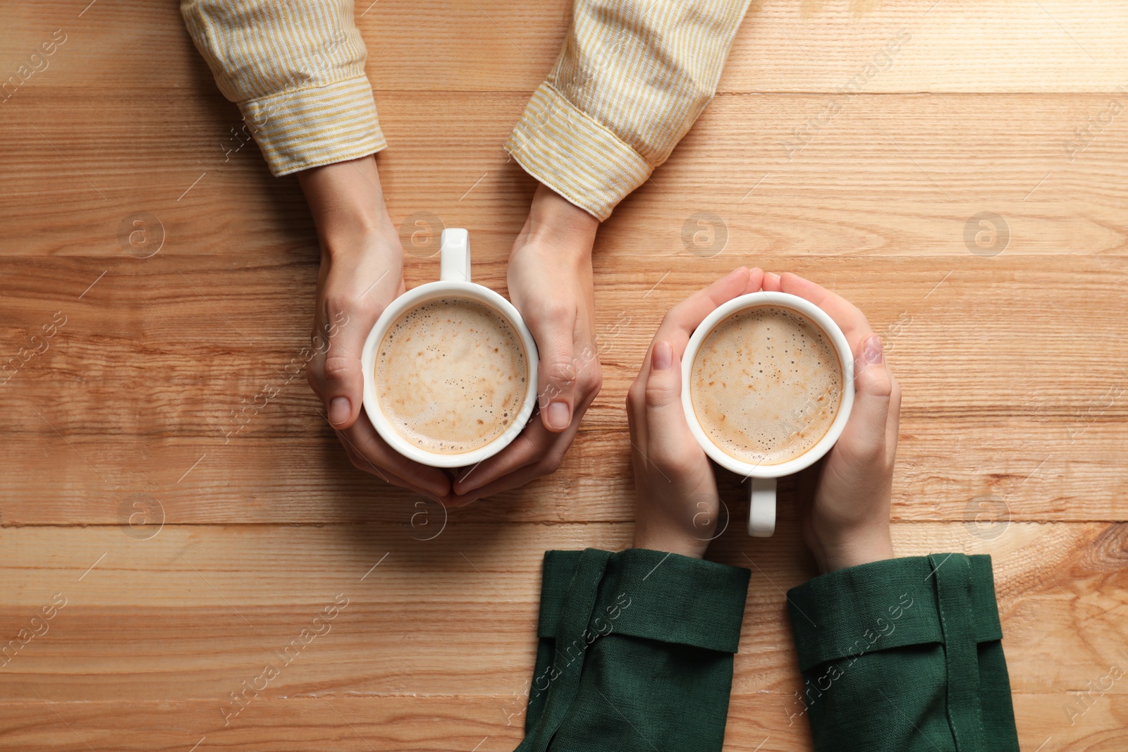 Photo of Women with cups of coffee at wooden table, top view