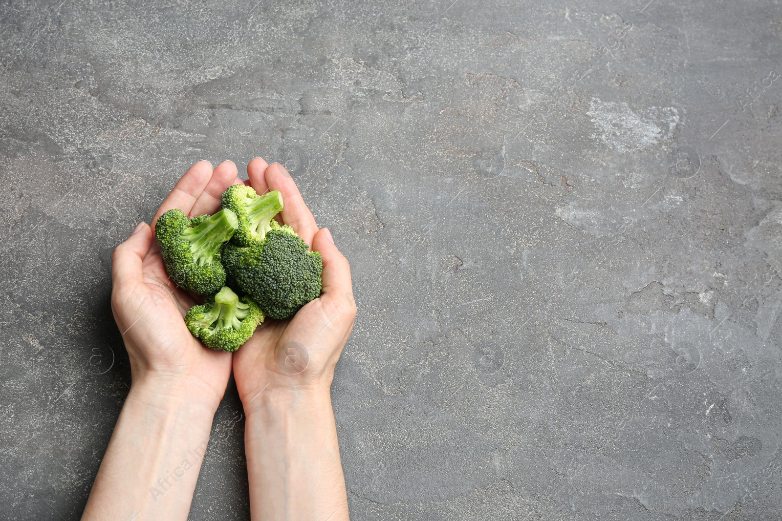 Photo of Female holding fresh green broccoli on grey stone table, top view. Space for text