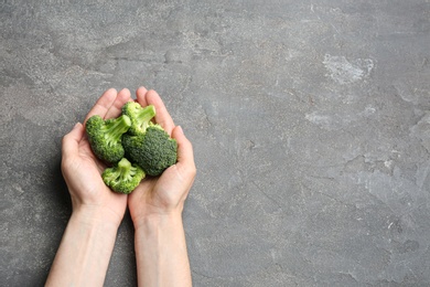 Photo of Female holding fresh green broccoli on grey stone table, top view. Space for text