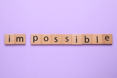 Photo of Motivation concept. Changing word from Impossible into Possible by removing wooden squares with letters I and M on violet background, top view