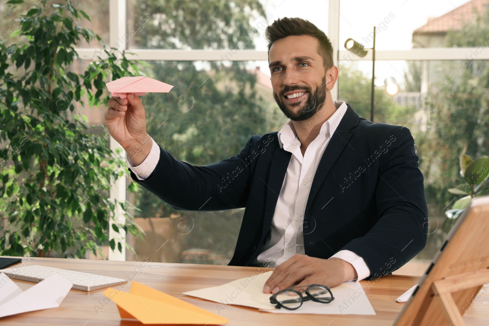 Photo of Handsome businessman playing with paper plane at desk in office