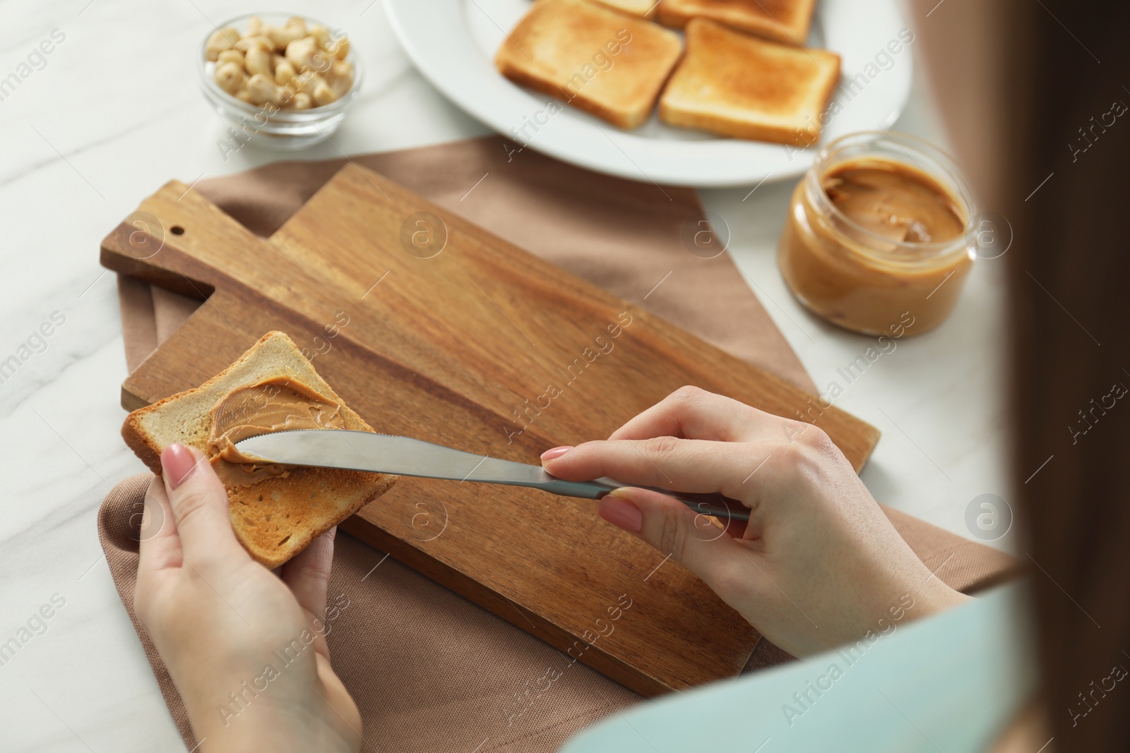 Photo of Woman spreading tasty nut butter onto toast at white table, closeup