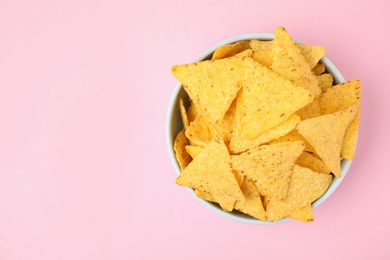 Bowl with tasty Mexican nachos chips on pink background, top view. Space for text