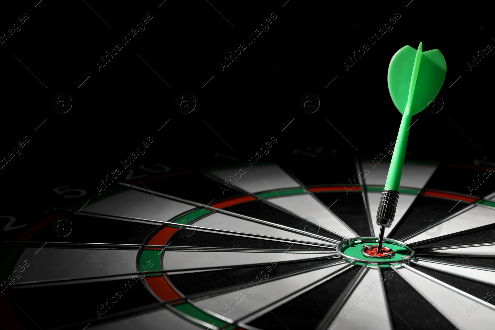 Photo of Green arrow hitting target on dart board against black background. Space for text