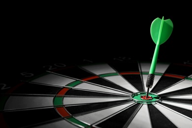 Photo of Green arrow hitting target on dart board against black background. Space for text