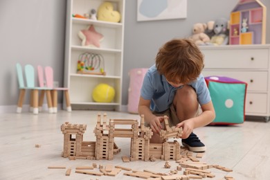 Little boy playing with wooden construction set on floor in room, space for text. Child's toy