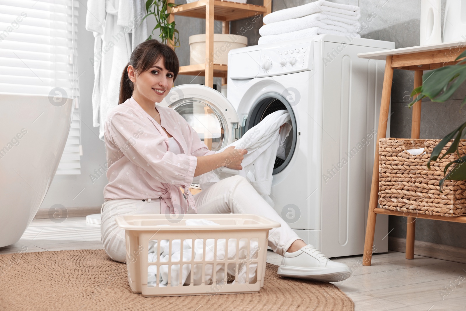 Photo of Happy young housewife putting laundry into washing machine at home