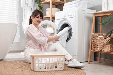 Happy young housewife putting laundry into washing machine at home