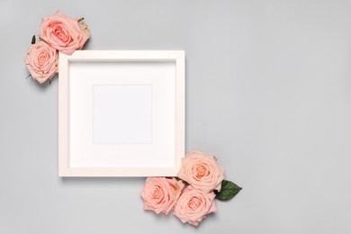 Photo of Empty photo frame and beautiful rose flowers on light gray background, flat lay. Space for text